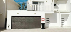 Un bâtiment à deux étages doté d’une porte de garage, d’un balcon avec des balustrades et d’une poubelle.