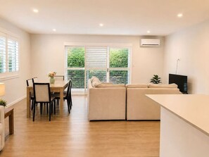 A modern living room with a sofa, a dining table with chairs, and a TV.
