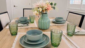 Ein Esstisch ist gedeckt mit grünem Glas, Tellern und einer Vase mit Blumen.