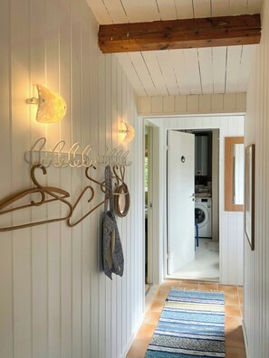 A hallway with wooden beams, a coat rack, wall-mounted lights, and a view into a laundry room. - Summer house near Ahl Beach and Ebeltoft (Ebeltoft)