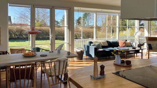 Ein geräumiger Wohnbereich mit Esstisch, Stühlen, einer Couch und einem großen Fenster mit Blick ins Freie.