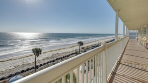 Vista de la playa desde un balcón techado con terraza de madera y barandillas blancas.