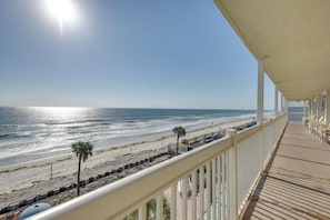 Blick auf den Strand von einem überdachten Balkon mit Holzdeck und weißen Geländern.