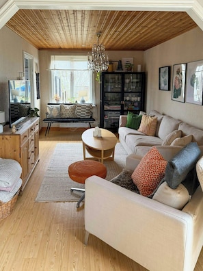 Ein gemütliches Wohnzimmer mit Holzbalkendecke, einer Couch, einem Couchtisch, einer Kommode und einem Fernseher.