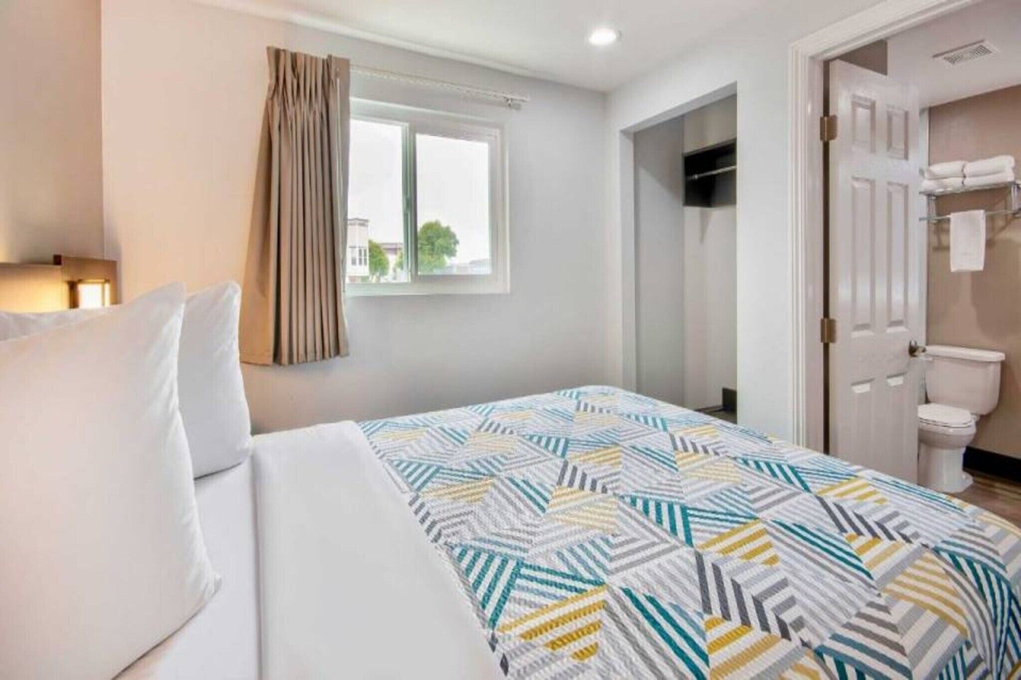 Een hotelkamer met een bed, een raam met gordijnen, een deur naar een badkamer en uitzicht op buiten.