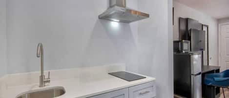 A modern kitchen with a stainless steel sink, a built-in range hood, and a compact refrigerator.