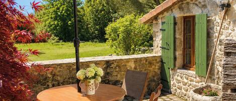 An outdoor patio with a round table, two chairs, a beige umbrella, and a stone wall.