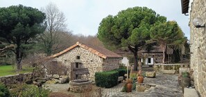 A stone building with a tiled roof, surrounded by trees and a stone pathway. - Cottage in former bakery in Dordogne (Saint-Estèphe)