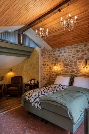 A bedroom with a stone wall, a wooden ceiling, a bed, a chair, and a nightstand. - Cottage in former bakery in Dordogne (Saint-Estèphe)