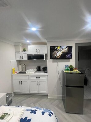 Una cucina compatta con mobili bianchi, un forno a microonde e un frigorifero. Una TV a schermo piatto è montata a parete sopra il bancone.