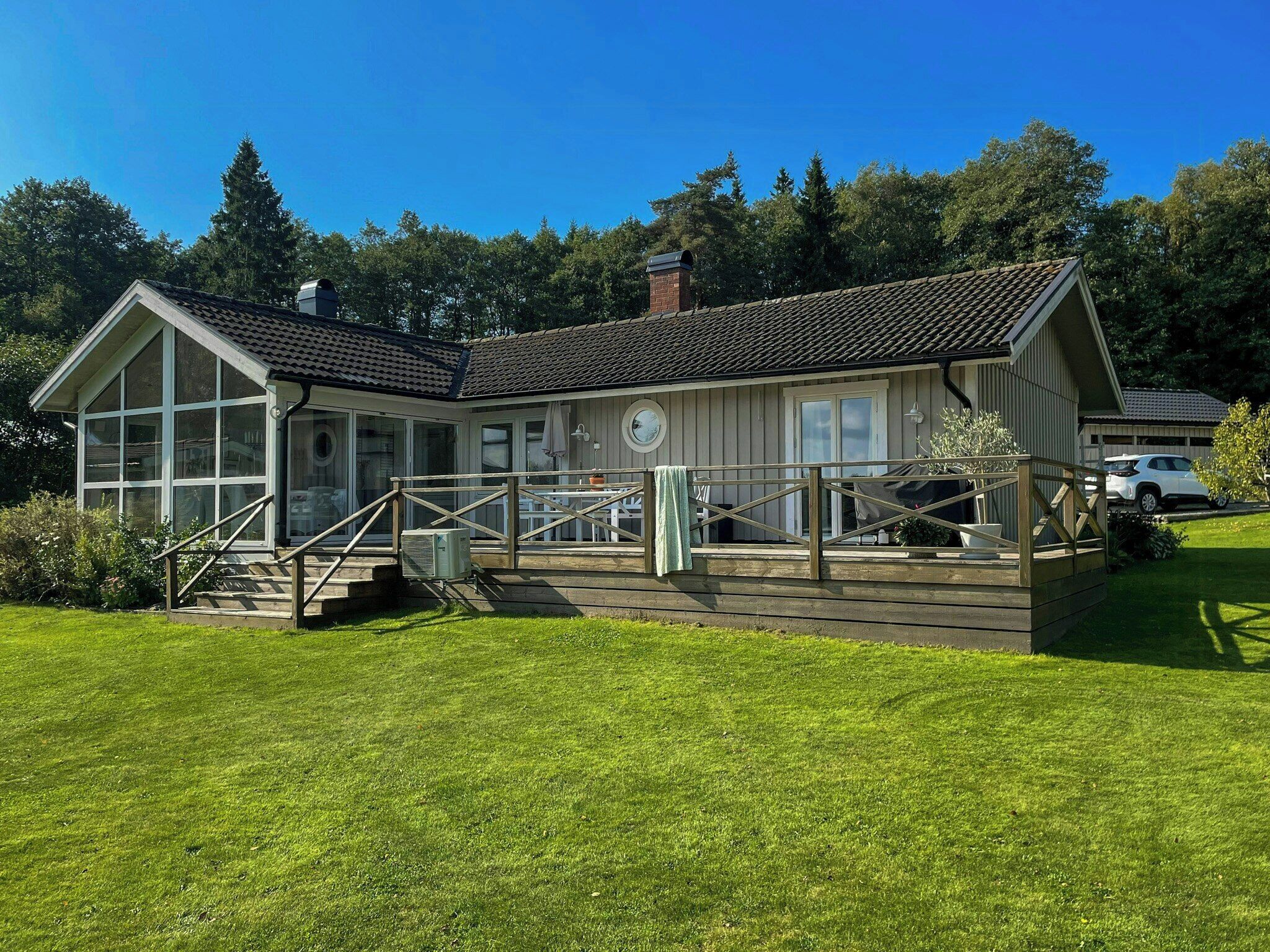 A two-story building with a covered porch, a small outdoor seating area, and a large windowed room.