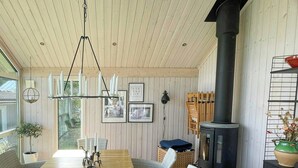 A long wooden dining table with wicker chairs, a hanging light fixture, a black stove, and framed pictures on the wall. - Lake cottage with private pier at Lake Nömmen (Stensjön)