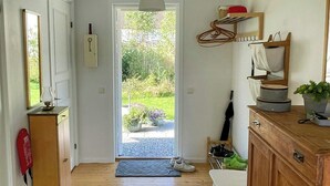A hallway with wooden flooring, a green rug, a white chair, a wooden cabinet, and a door leading outside. - Lake cottage with private pier at Lake Nömmen (Stensjön)