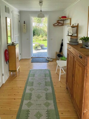 A hallway with wooden flooring, a green rug, a white chair, a wooden cabinet, and a door leading outside. - Lake cottage with private pier at Lake Nömmen (Stensjön)
