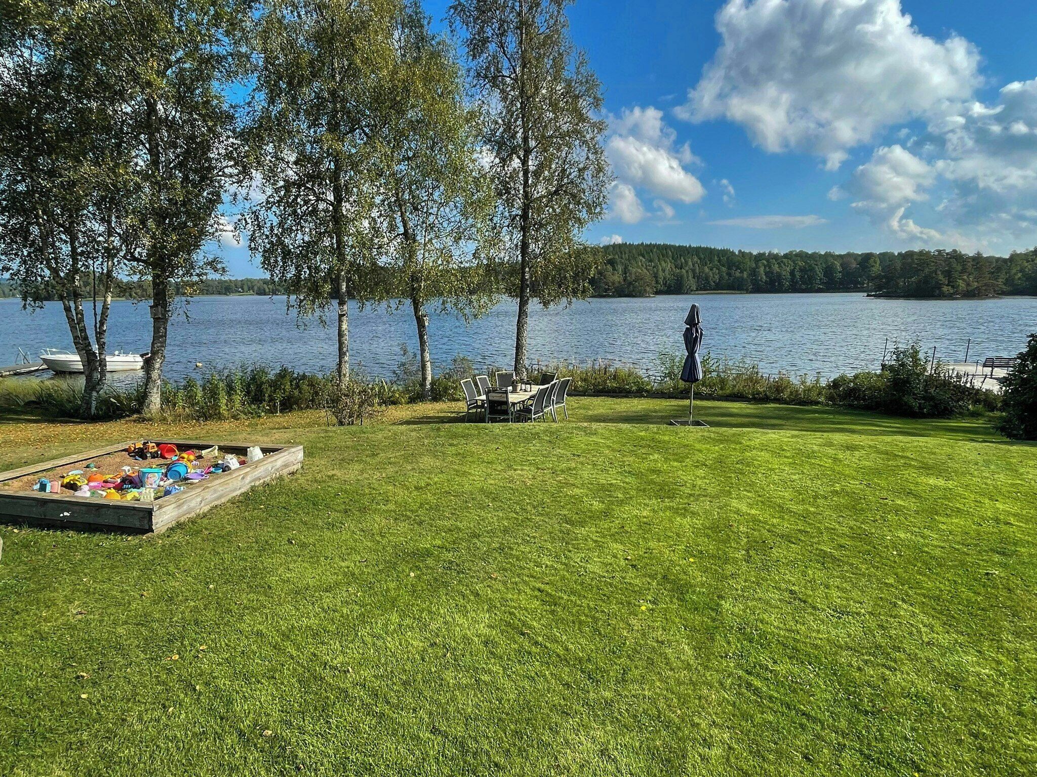 Un espace verdoyant avec une table et des chaises, un petit bateau et une vue sur le lac.