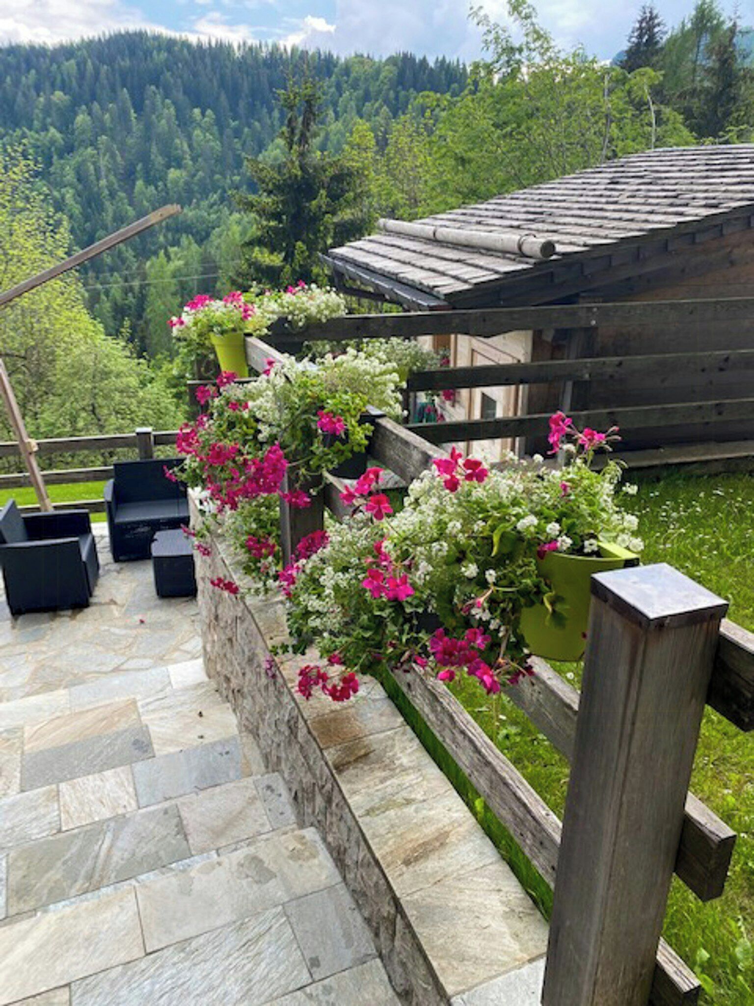 A stone staircase leading to a wooden deck with outdoor seating and flower planters.