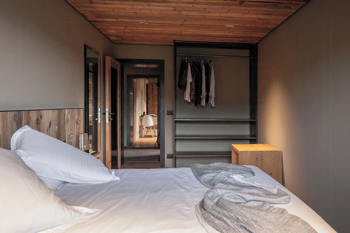 A bedroom with a bed, a wooden headboard, a wardrobe, and a small wooden stool.