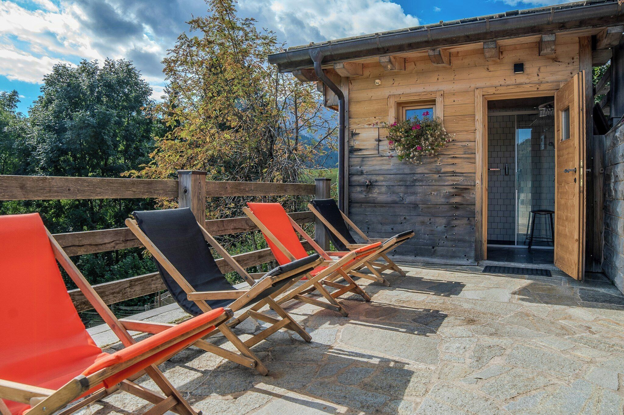 A wooden cabin with a stone patio, a wooden fence, and a door leading to a bathroom.