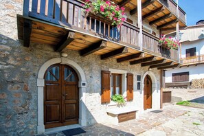 A stone building with wooden balconies, arched doors, and potted plants. - Historic dwelling with terrace in Sauris (Sauris di Sopra)