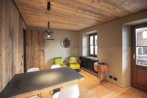 Une pièce avec un plafond en bois, un miroir rond, une table avec des chaises et une fenêtre.