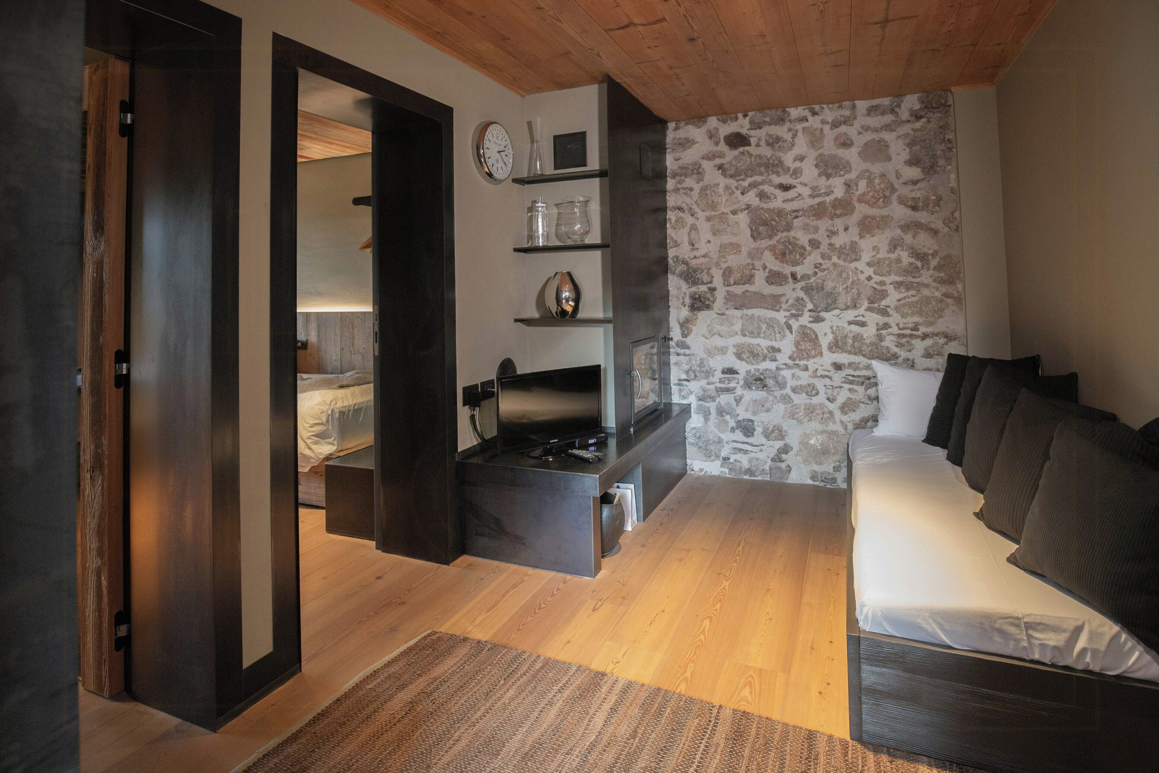 A modern room with a stone wall, a bed, a sofa, and a built-in stove.