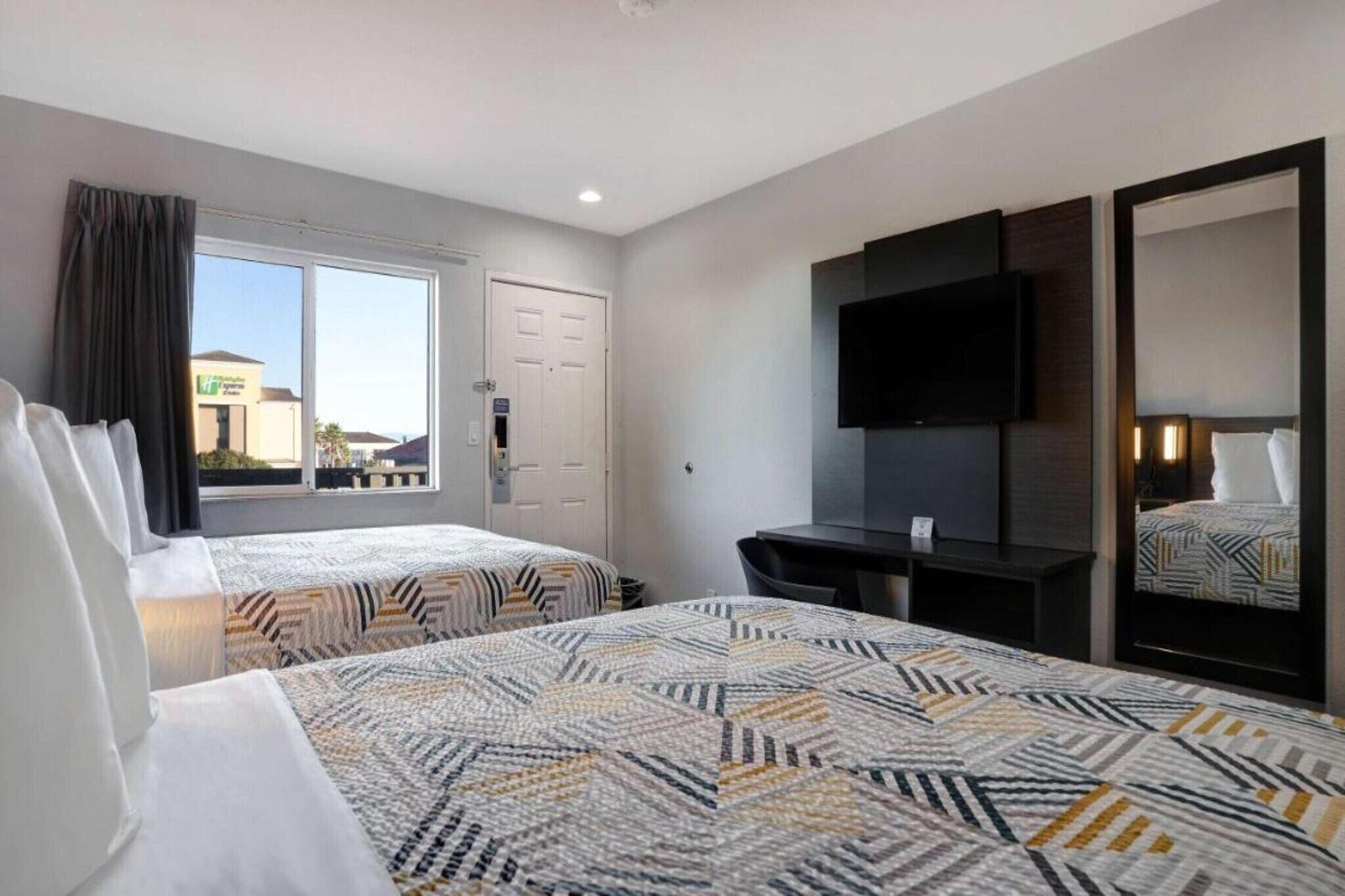 A hotel room with two beds, a desk, a TV, and a large window.