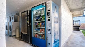 Eine Reihe von Verkaufsautomaten mit blau-silbernem Design, gelegen in einem Außenbereich mit Betonboden und einer Wand.
