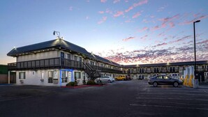 Un motel con aparcamiento, una escalera al nivel superior y una fila de habitaciones con techo plano.