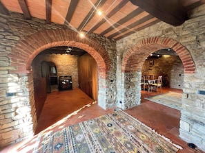 Ein Innenraum mit Steinwänden, rundbogigen Durchgängen, einem gemusterten Teppich und einem Kamin.