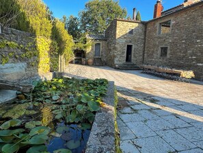 Ein Steinhaus mit Innenhof, einem kleinen Teich mit Seerosen und Sitzgelegenheiten im Freien.