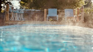Ein Schwimmbecken mit klarem Wasser, umgeben von einer Holzterrasse und zwei Liegestühlen.