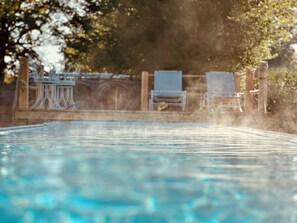 Ein Schwimmbecken mit klarem Wasser, umgeben von einer Holzterrasse und zwei Liegestühlen.