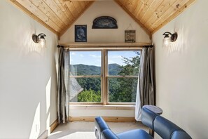 A room with a large window, wooden ceiling, and a view of green hills. - Spa + Game Room | Deck + Views | Short Drive to Pigeon Forge | Serenity Ridge (Sevierville)