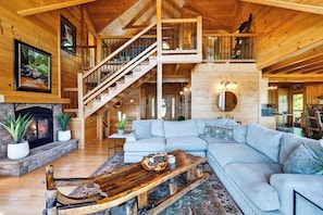 A spacious log cabin interior with a large living room, a fireplace, a staircase, and a dining area. - Spa + Game Room | Deck + Views | Short Drive to Pigeon Forge | Serenity Ridge (Sevierville)