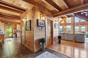 A wooden cabin interior with a kitchen, dining area, and a large window overlooking a scenic landscape. - Spa + Game Room | Deck + Views | Short Drive to Pigeon Forge | Serenity Ridge (Sevierville)