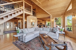 A wooden interior with a staircase, a sectional sofa, a coffee table, and a dining table. - Spa + Game Room | Deck + Views | Short Drive to Pigeon Forge | Serenity Ridge (Sevierville)