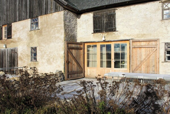 Un bâtiment rustique avec un mur en pierre, des portes en bois et une table dressée pour le repas.