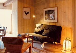 Une pièce chaleureuse avec un mur en bois, un canapé, un fauteuil en osier, une table avec des livres et un lampadaire.
