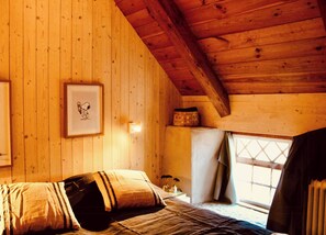 Une pièce de style cabane en bois, avec un lit, un tableau encadré au mur et une fenêtre avec des rideaux.