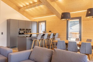 Eine moderne Küche mit grauen Schränken und einem Essbereich mit Holztisch und grauen Stühlen.