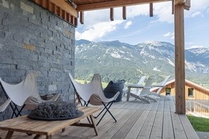 Eine Holzterrasse mit einer Steinsäule, Sitzgelegenheiten im Freien und Blick auf die Berge.