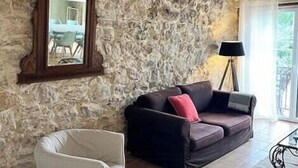 Eine Steinsäule, ein spiegel mit Holzrahmen, ein dunkles Sofa mit roten Kissen, ein weißer Sessel und eine Stehlampe.