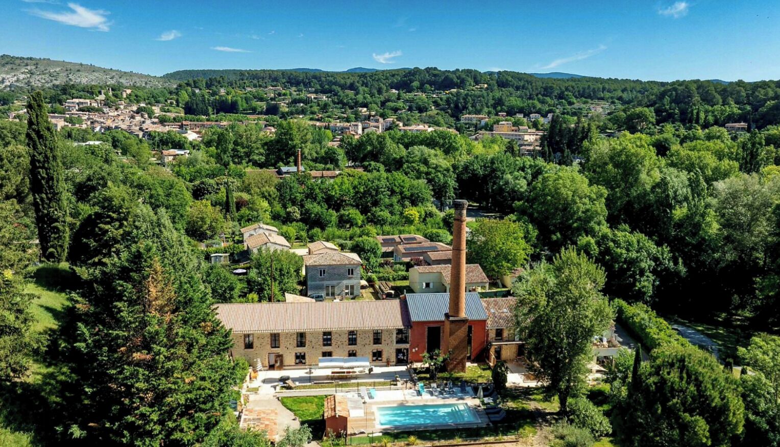 Un hotel con piscina, immerso nel verde e con le montagne sullo sfondo.