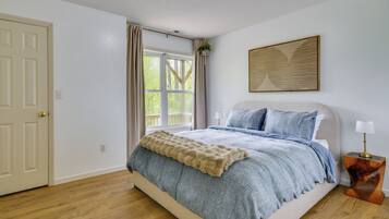 Une chambre à coucher avec un lit, une fenêtre avec des rideaux, une table de chevet avec une lampe et une œuvre d’art accrochée au mur.