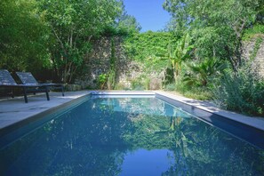 Ein Pool mit Steinmauer und üppiger, umgebender Bepflanzung.