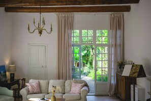 Ein Zimmer mit einem weißen Sofa, einer Chandelierleuchtre, einer Tür und Blick auf Grünfläche draußen.