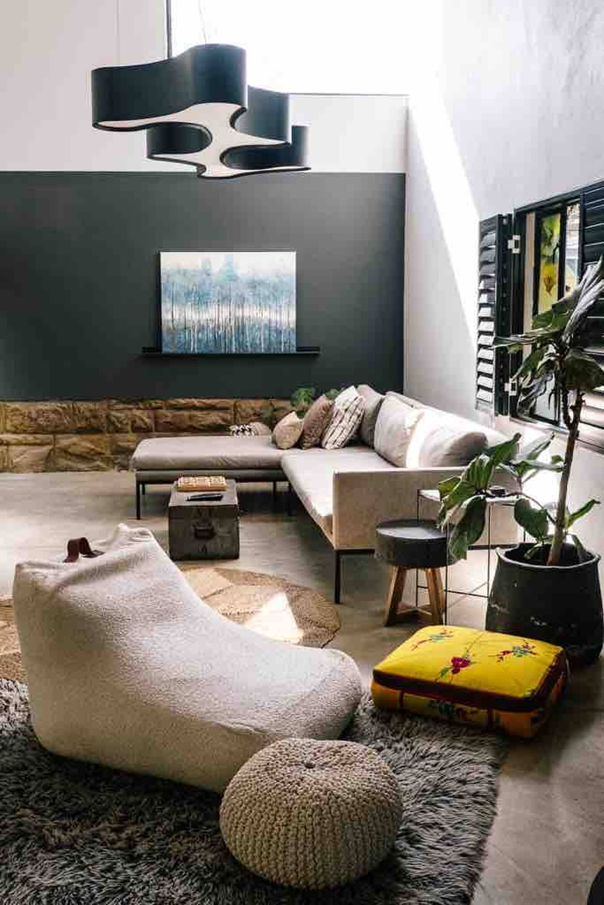 Un salon moderne comprenant un canapé, une table basse, un pouf, un tapis, une plante en pot et un tableau accroché au mur.