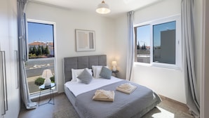 Una camera d'albergo con un letto, un comodino con una lampada, una finestra con tende e vista sugli edifici.