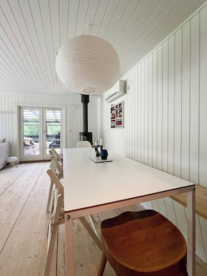 Ein Zimmer mit einem weißen Tisch, Holzsesseln, einer Pendelleuchte und Blick durch eine Glastür.