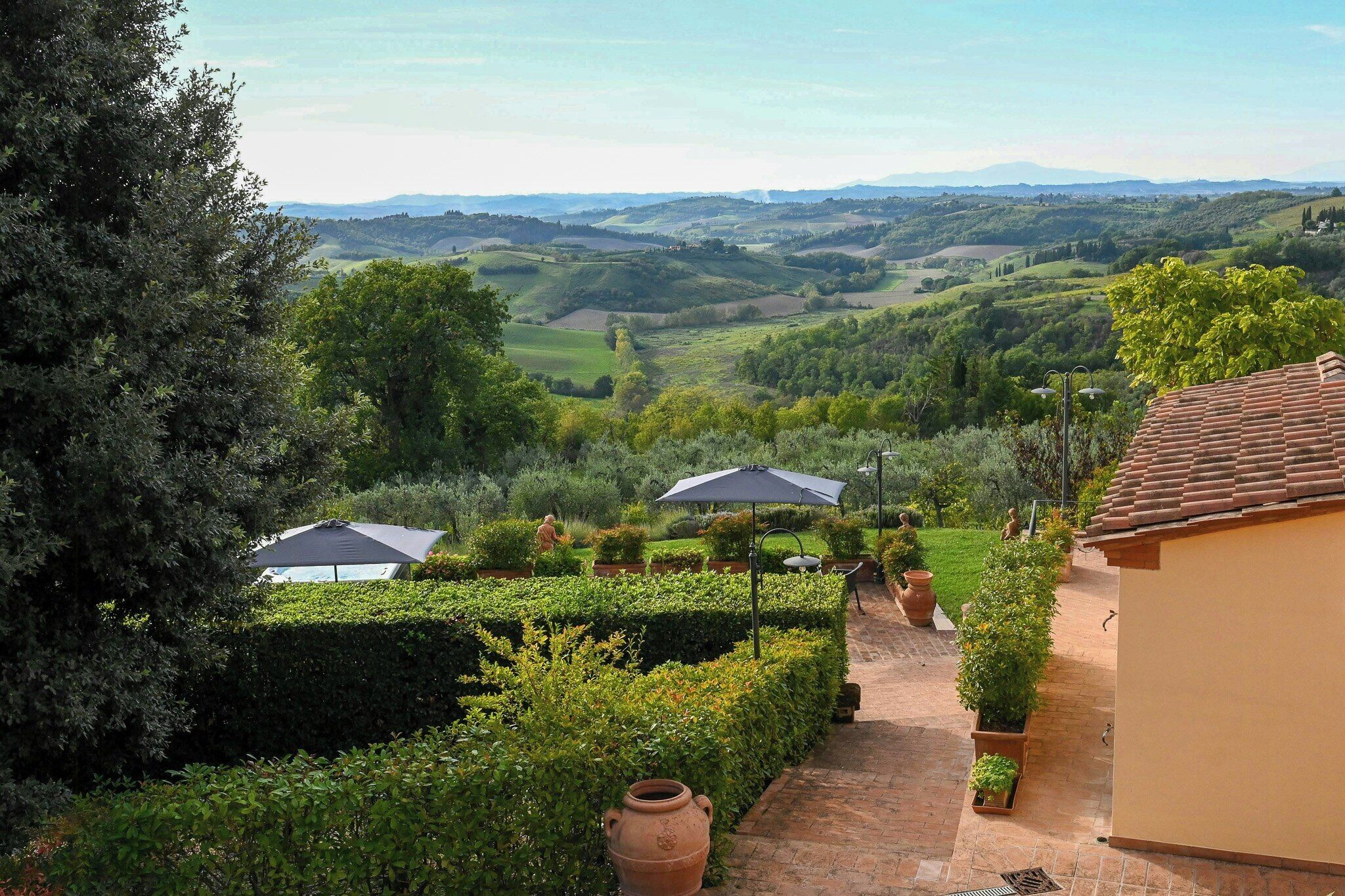 A garden with a pathway, a building with a tiled roof, and a view of rolling hills.